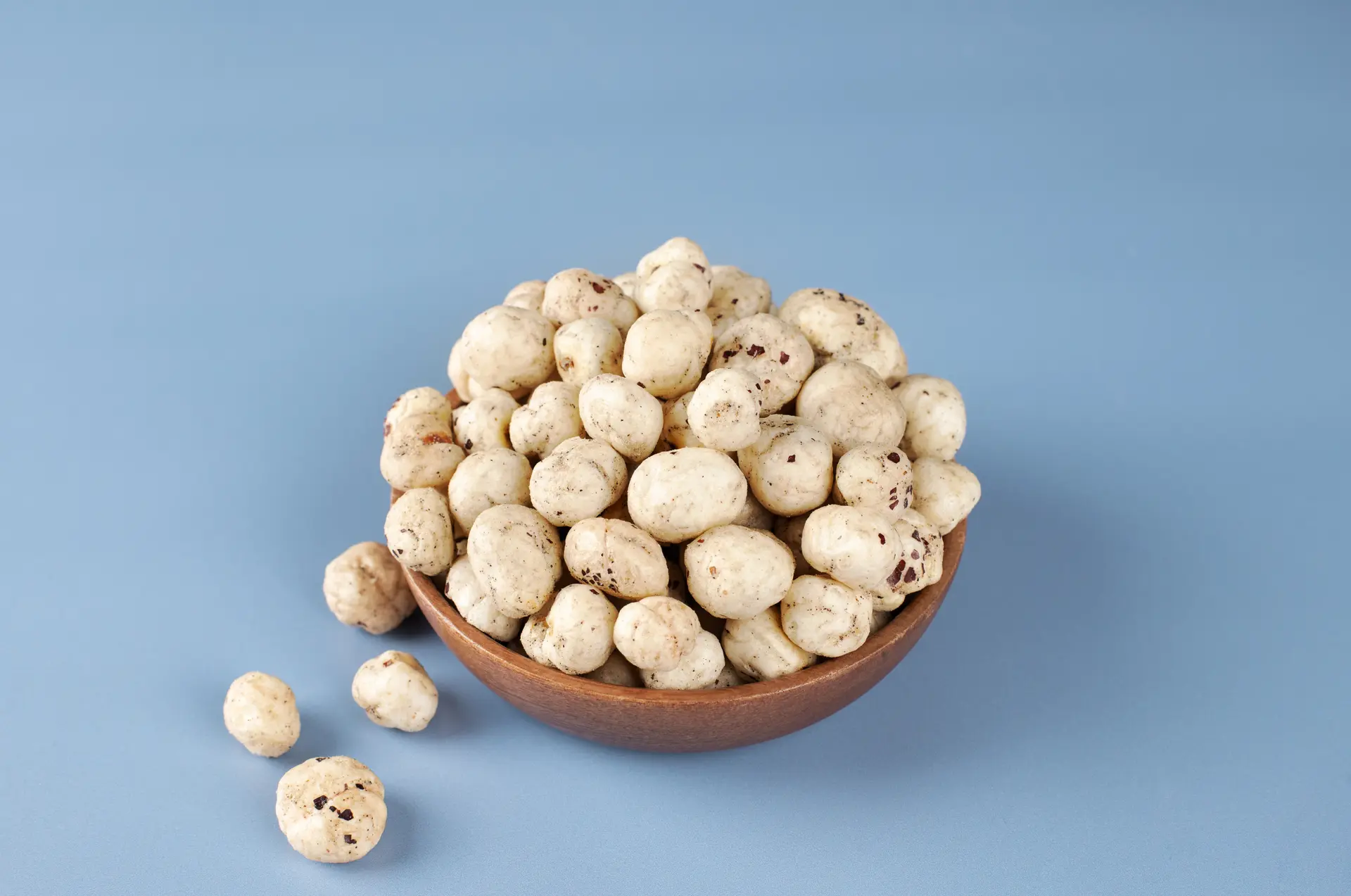 A wooden bowl of phool makhana on a soft blue background